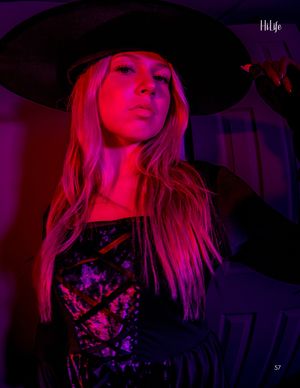 Dramatic fashion portrait in pink neon lighting with wide-brimmed black hat and floral design.