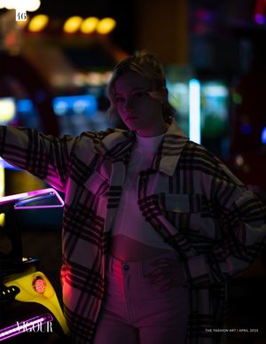 Nighttime portrait in plaid jacket illuminated by colorful neon lights and purple glow creating moody urban atmosphere.