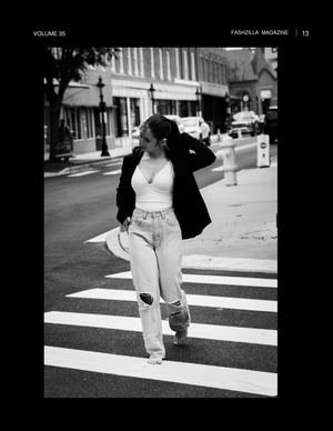 Black and white street photograph of someone crossing an urban crosswalk wearing a white tank top and casual pants.