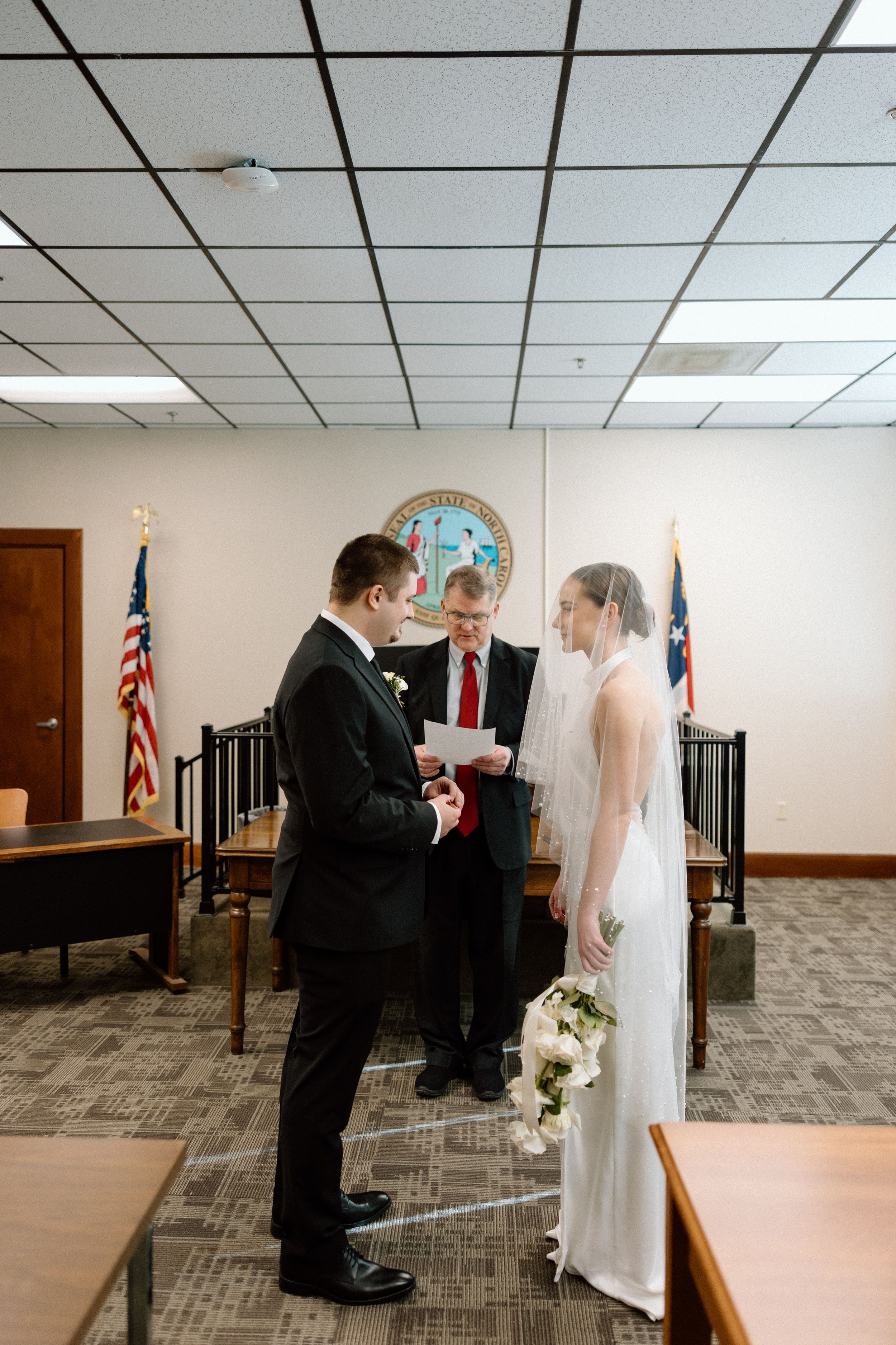 Civil ceremony in a courthouse with couple exchanging rings before an officiant.