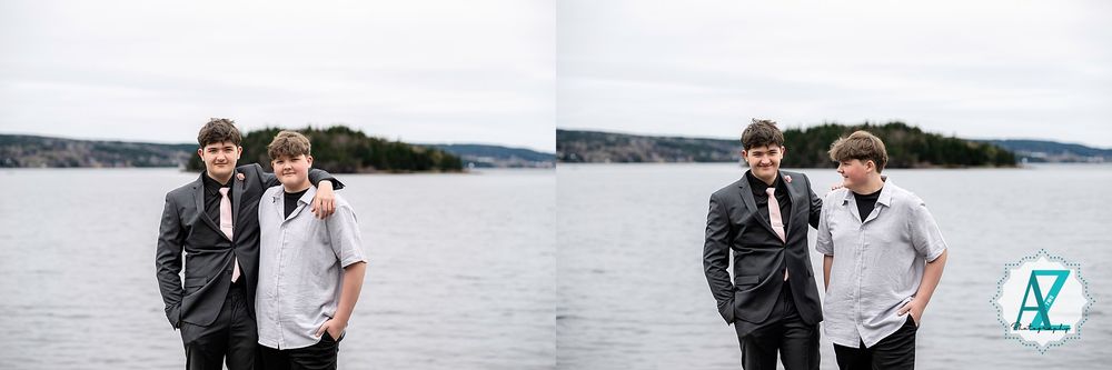 Two people in suits stand together by a lake on an overcast day against a wooded shoreline background.