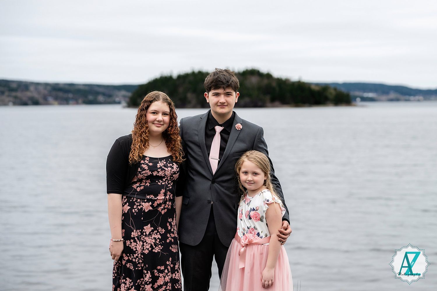 A family wearing formal attire poses together against a scenic waterfront backdrop near rolling hills.