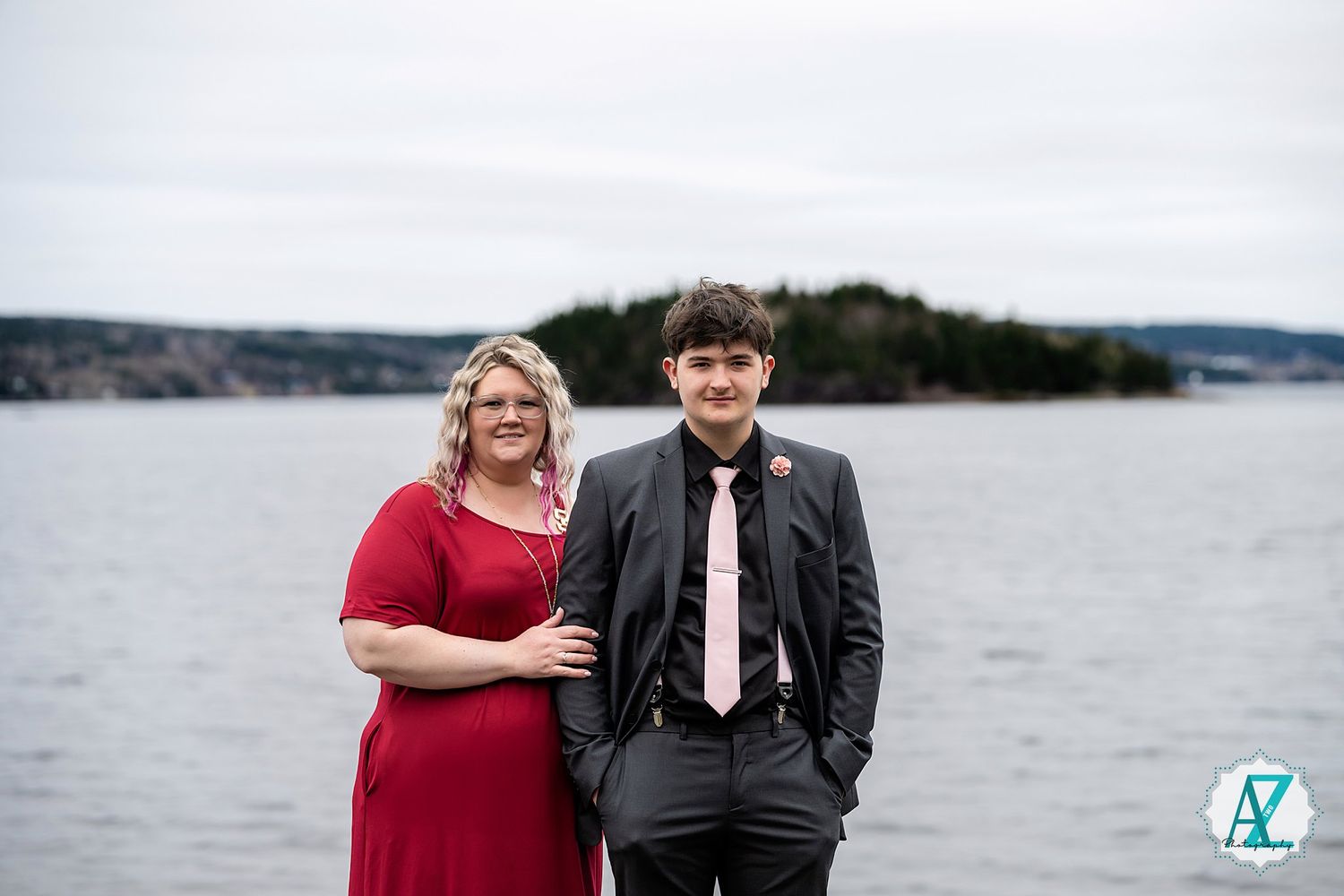 A couple poses together against a misty coastal backdrop with calm waters and distant islands.