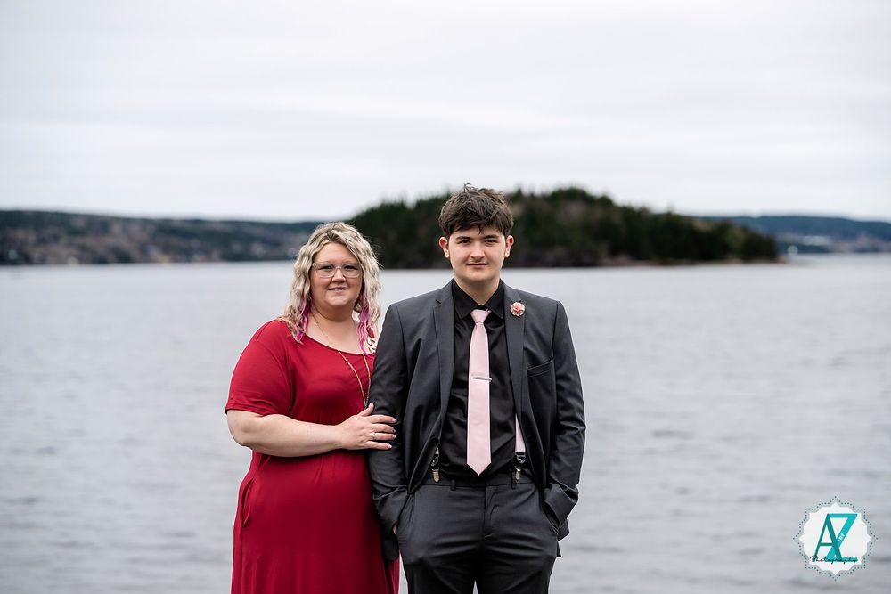 A couple poses together against a misty coastal backdrop with calm waters and distant islands.
