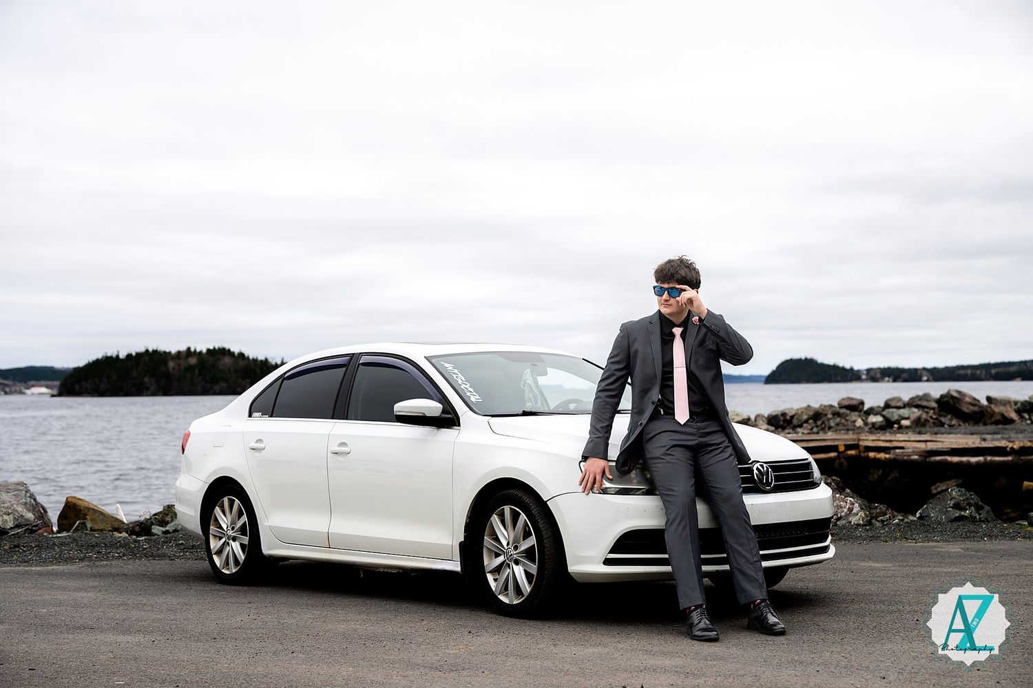 A white sedan parked along a rocky coastline with cloudy skies in the background.
