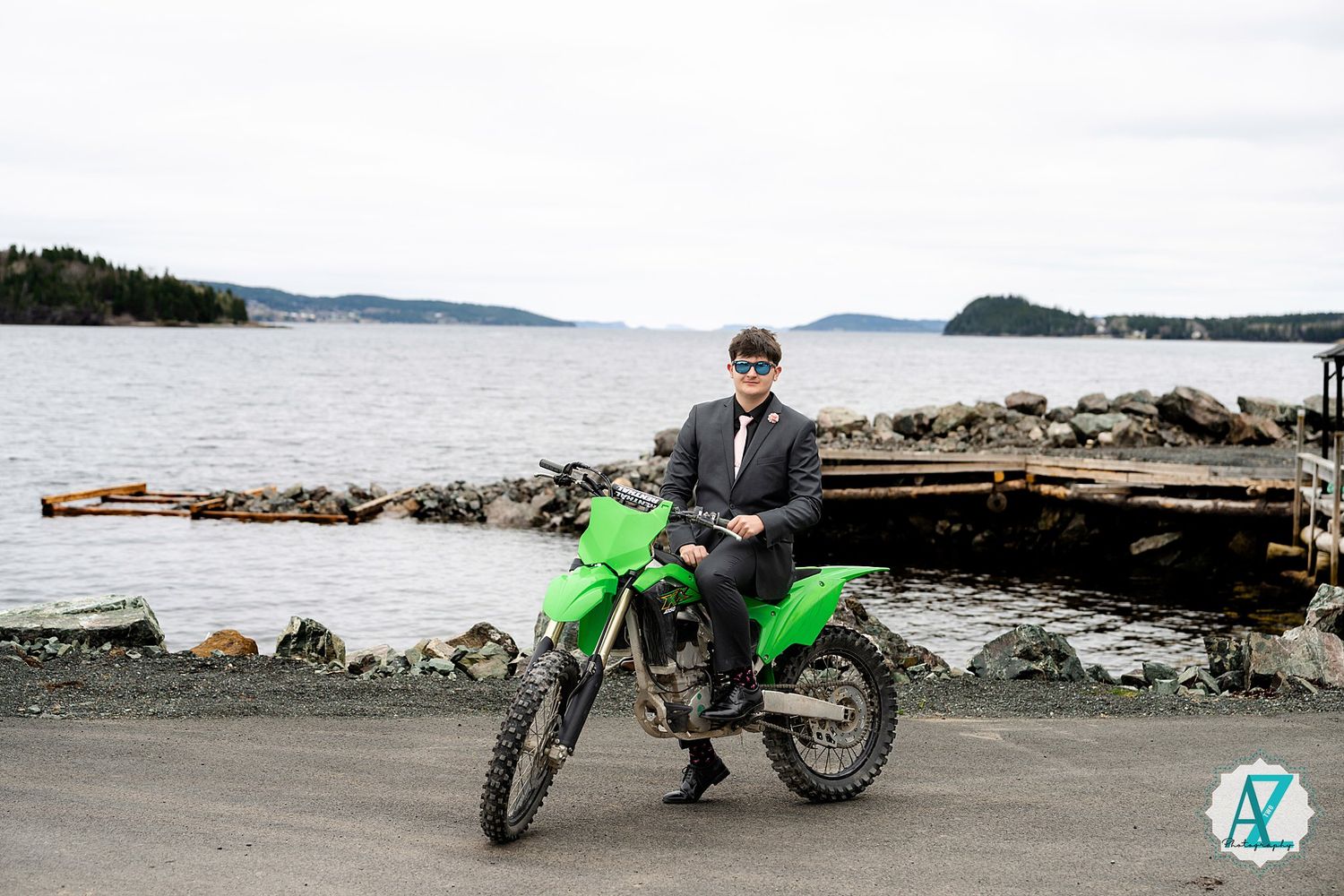 A bright green dirt bike parked near a rocky shoreline with islands and water visible in the background.