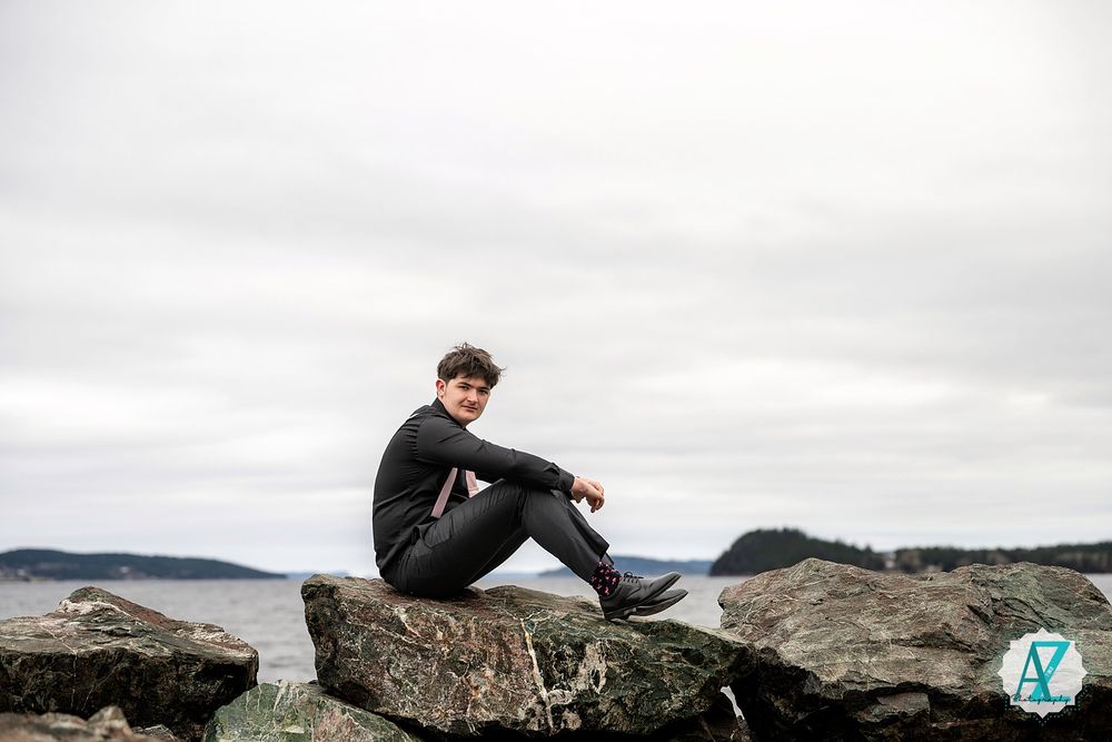Person sitting on coastal rocks overlooking water on a cloudy day in outdoor adventure scene.