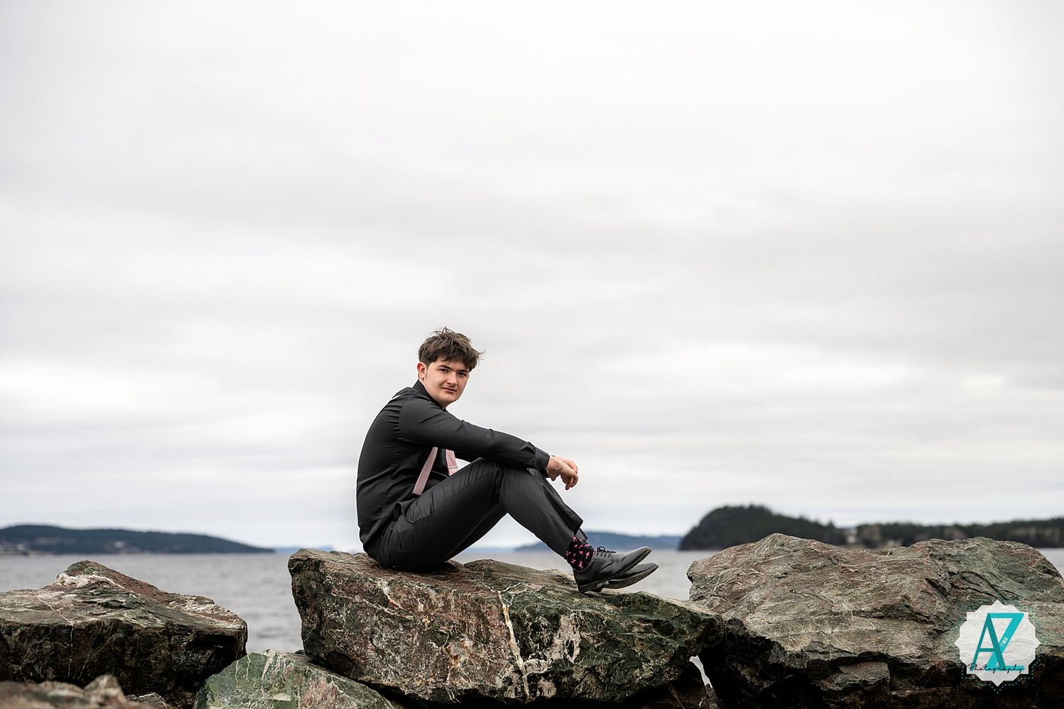 Person sitting on coastal rocks overlooking water on a cloudy day in outdoor adventure scene.