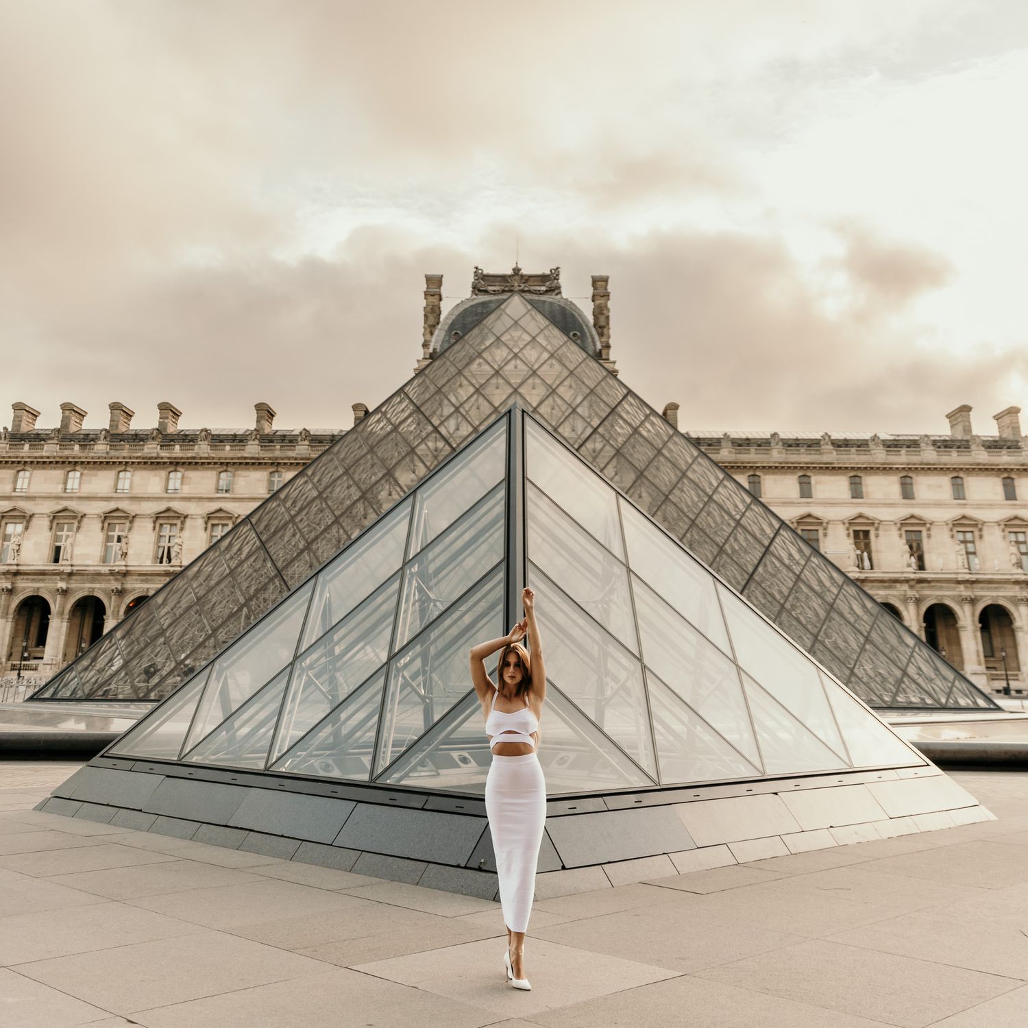 Artistic portrait at the Louvre pyramid featuring clean geometric lines and soft sepia tones.