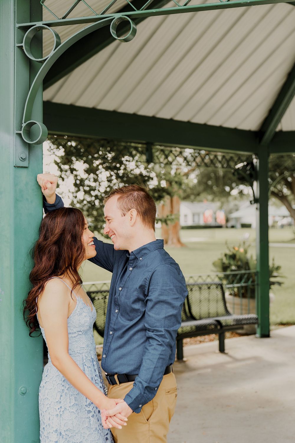 Romantic couple sharing a tender moment under a green gazebo in a park setting on a sunny day.