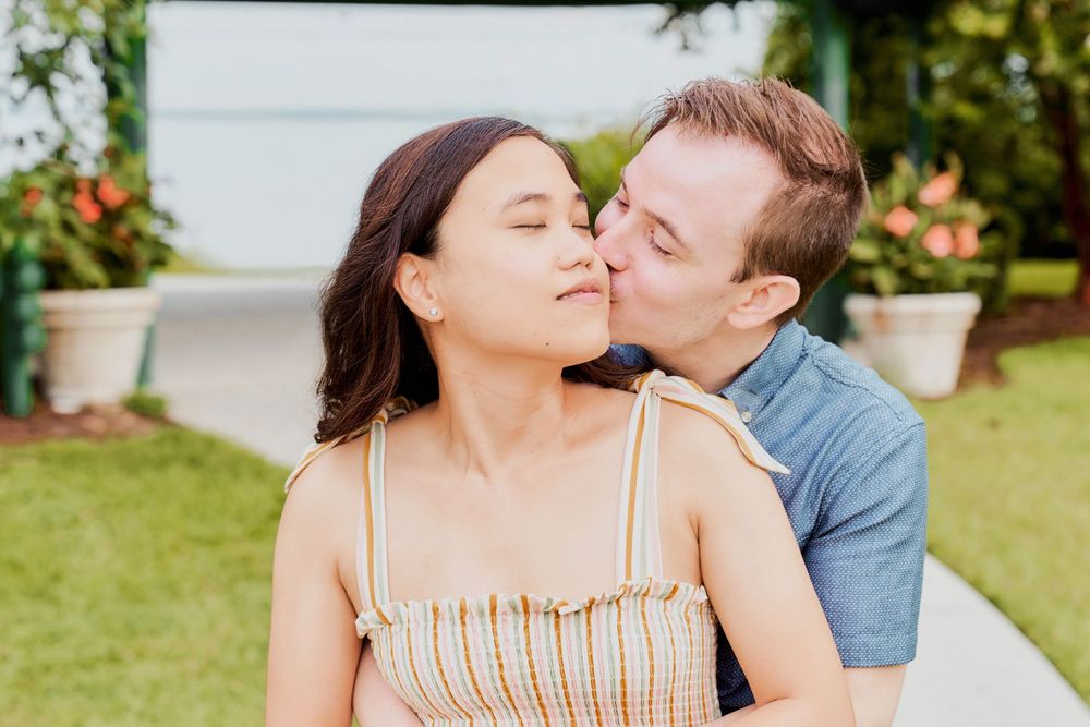 A couple shares an affectionate moment together while sitting outdoors in a garden setting.