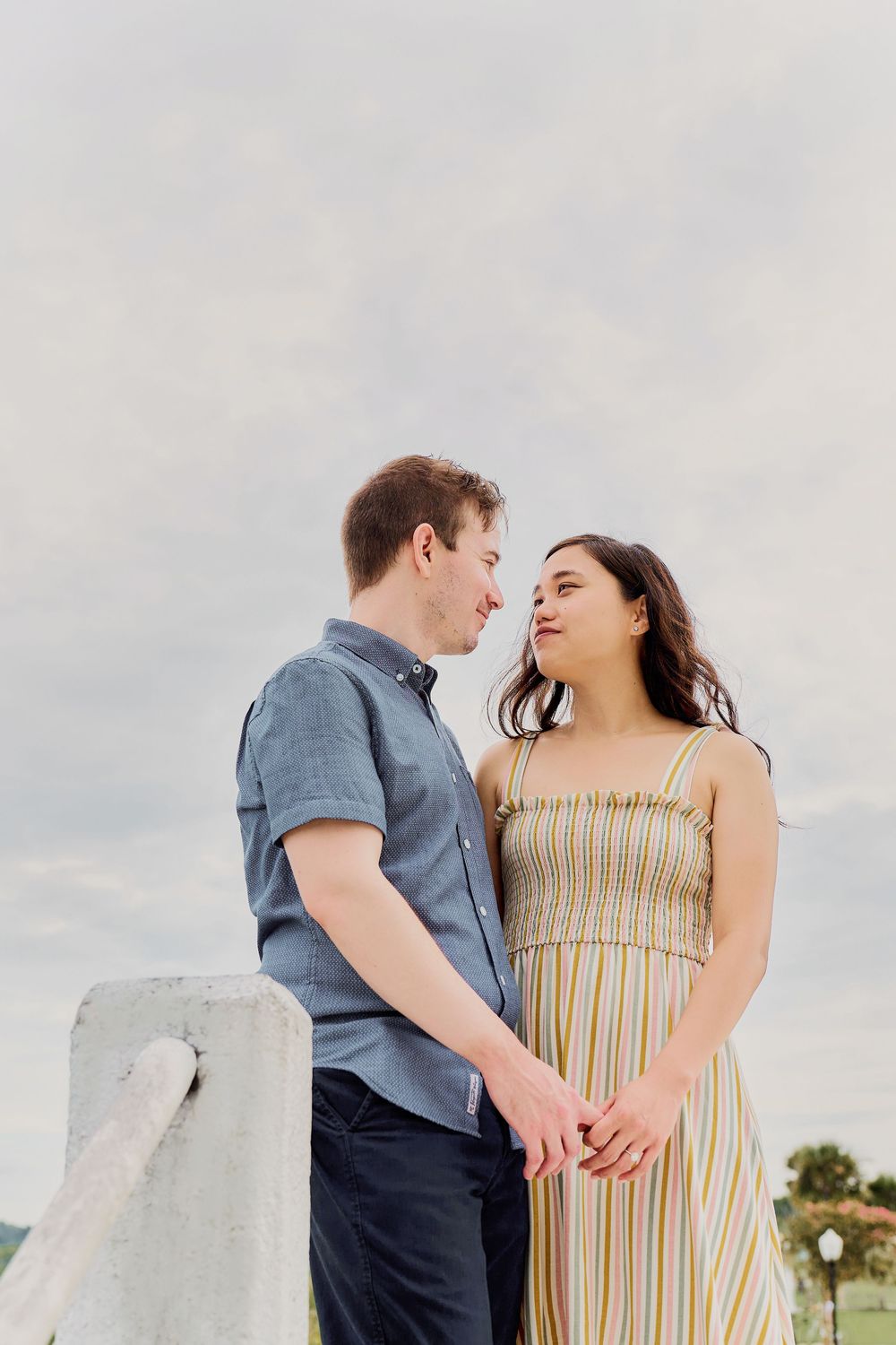 Couple sharing a romantic moment while holding hands against a cloudy sky at an outdoor location.
