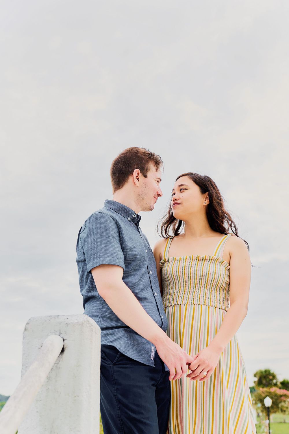 Couple sharing a romantic moment while holding hands against a cloudy sky at an outdoor location.