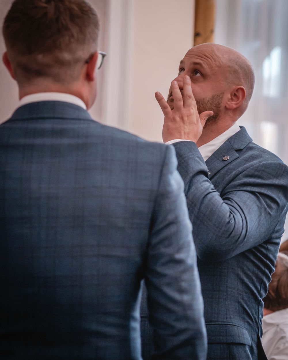 An emotional moment between two people in grey suits as one touches his face in what appears to be a touching reaction.
