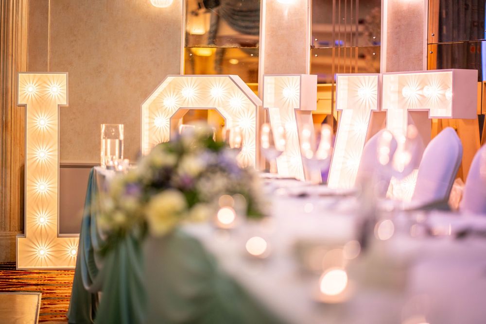 Elegant wedding reception table setting with illuminated LOVE marquee letters and soft candlelight decor.