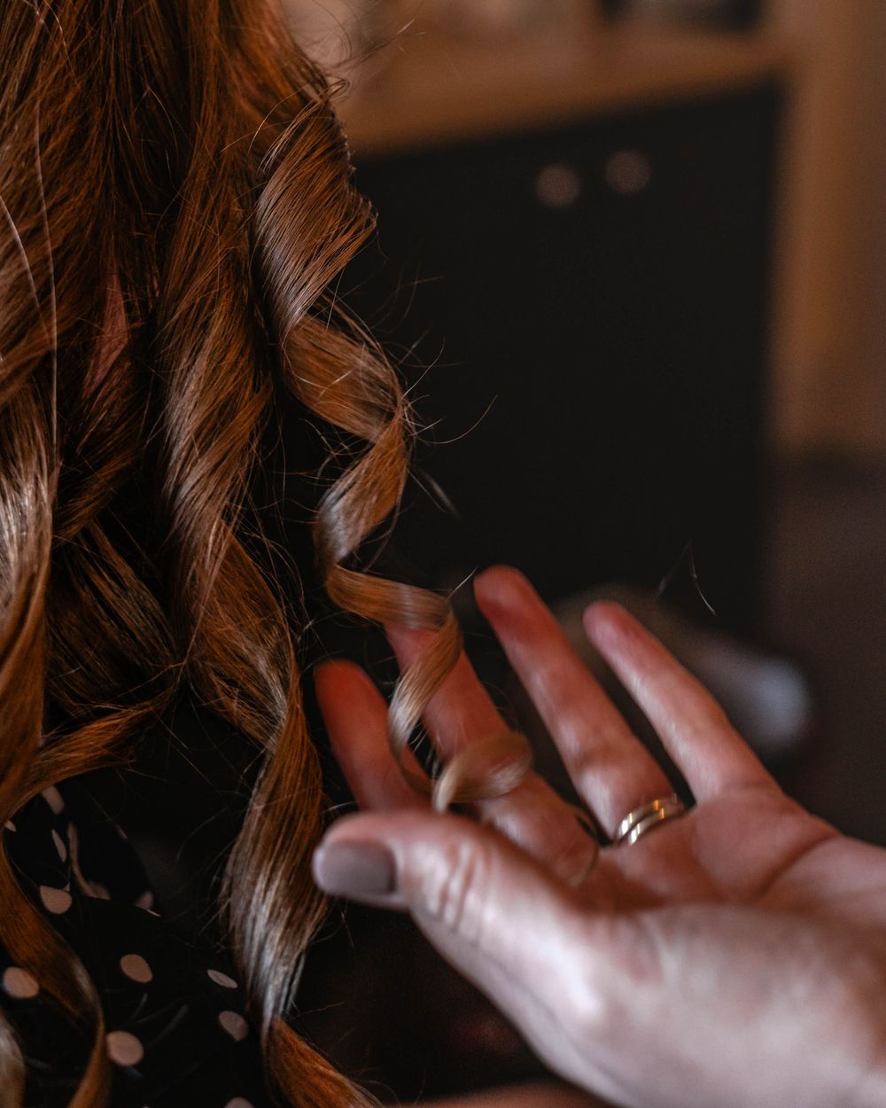 Close-up of curled brown hair with a hand wearing a ring gently touching the styled locks.