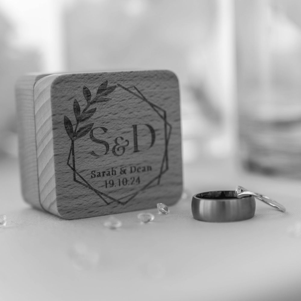 A black and white close-up photo of a wedding ring next to a personalized wooden coaster with monogram initials S&D.