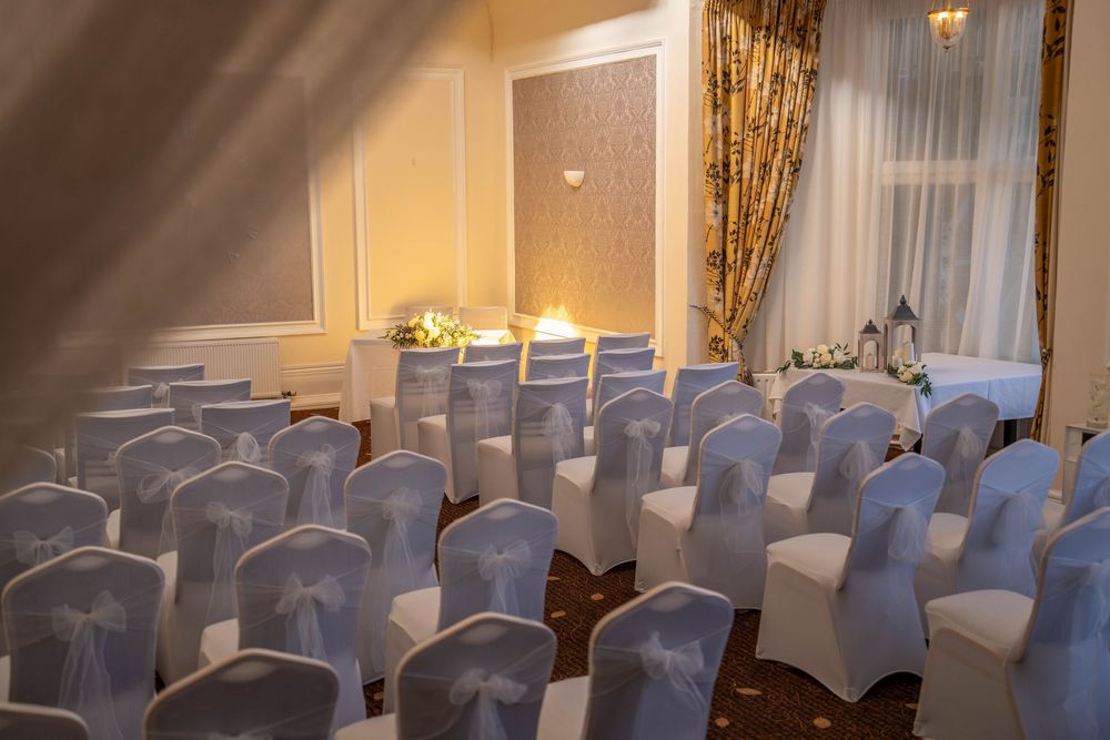 A wedding ceremony venue with rows of white chair covers and elegant draping in a softly lit banquet room.