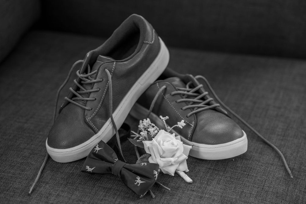 A pair of gray casual sneakers with white soles displayed with a small white rose on a dark textured surface.