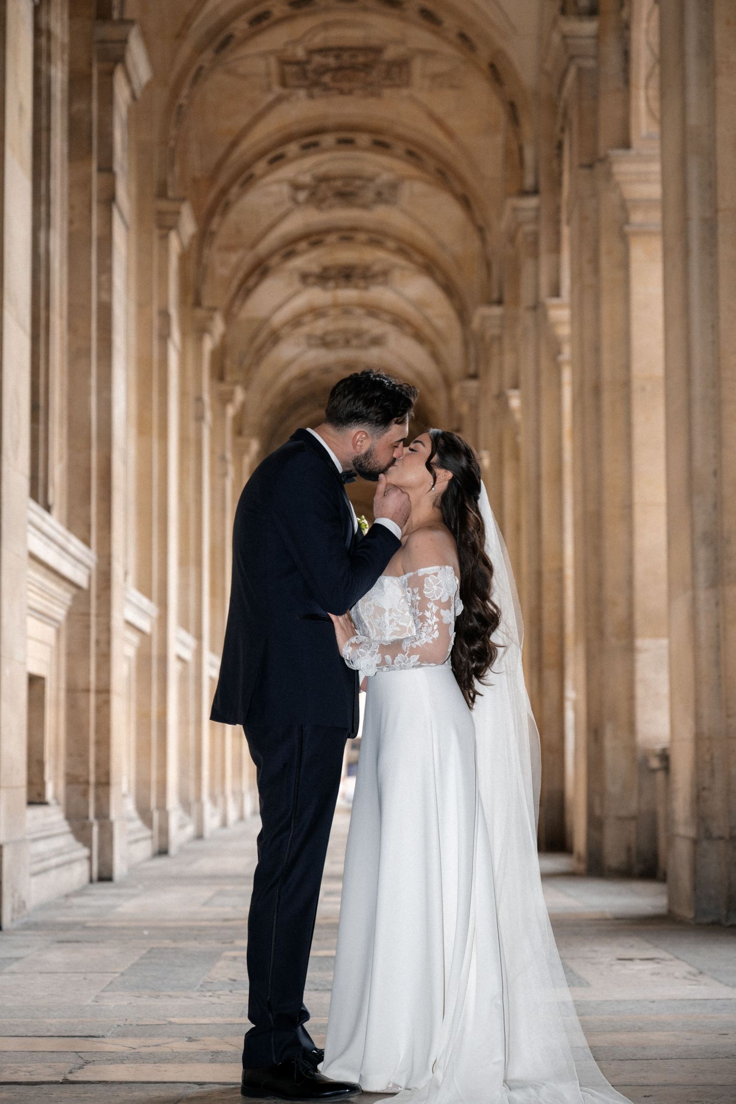 A couple dancing together under elegant stone archways with palm trees visible in the background.