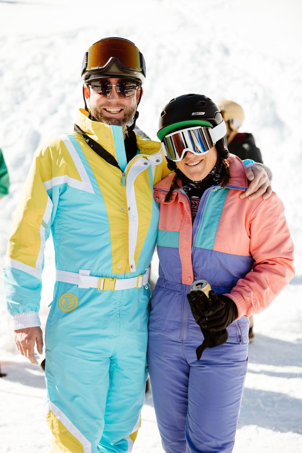 Skiers wearing colorful retro ski suits pose together on snowy slopes.