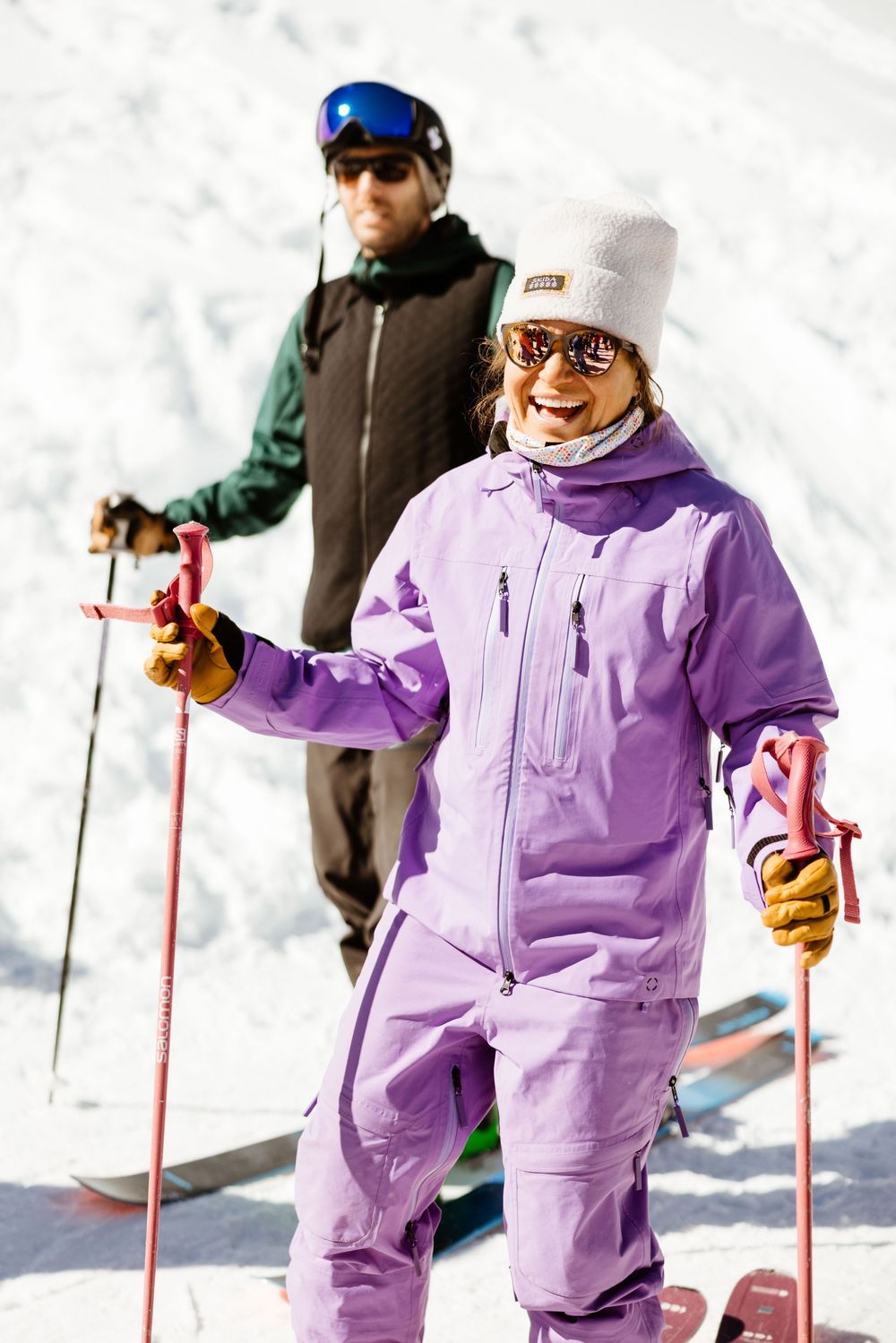 Skier wearing purple snowsuit and white beanie navigates down snowy mountain terrain.