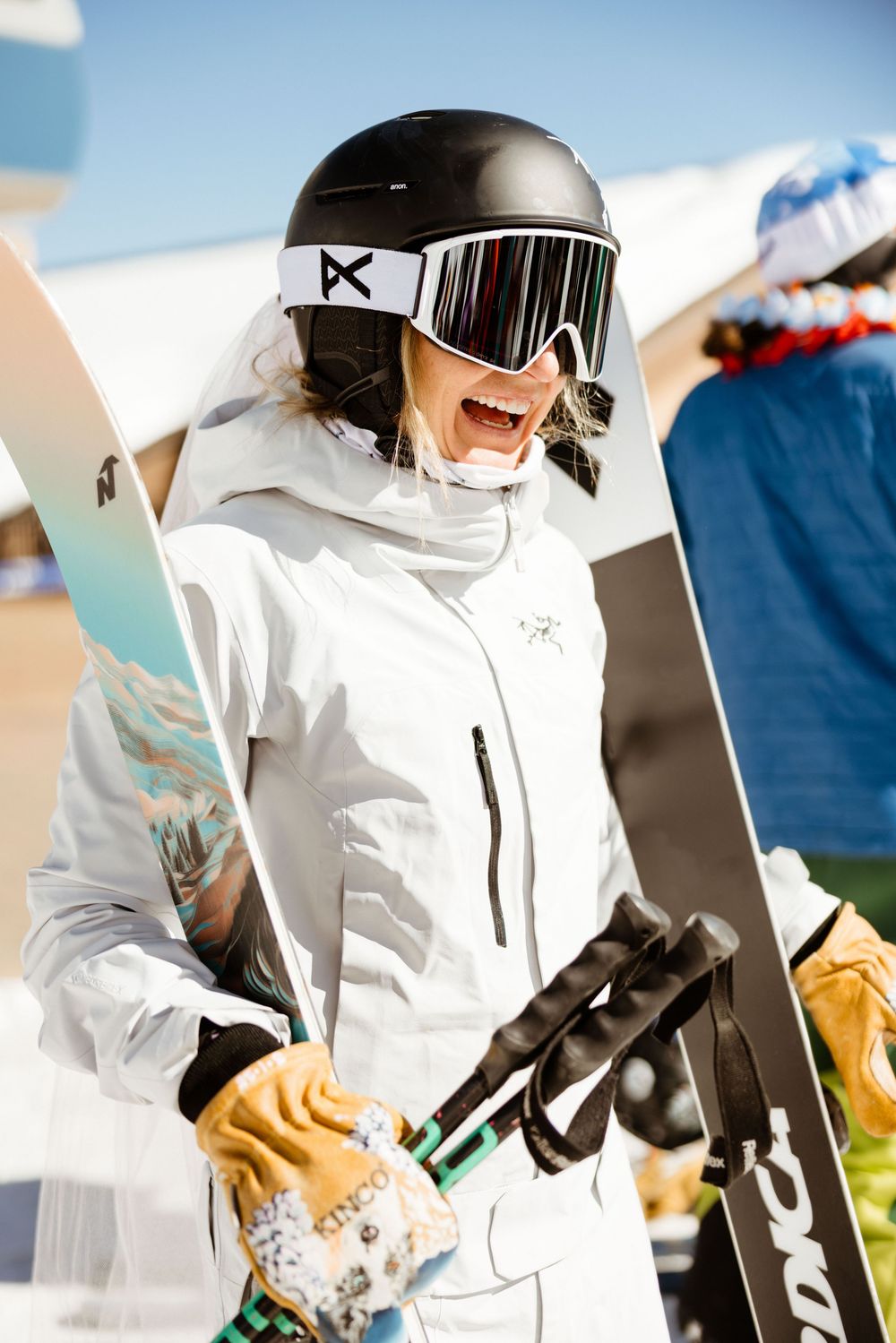 Skier in white winter gear and helmet prepares equipment on sunny slope.