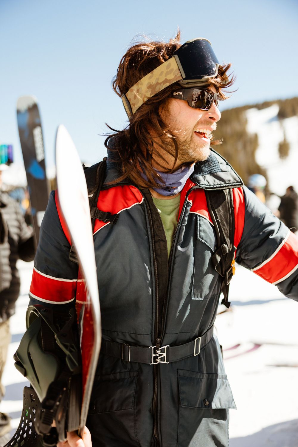 Skier in black and red winter jacket gestures while standing in snowy terrain.