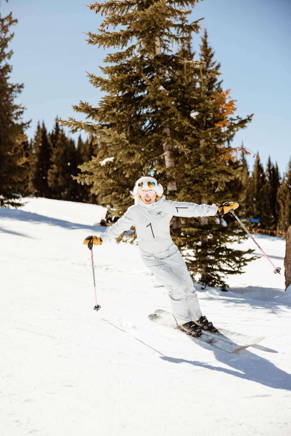 Skier carves through fresh powder snow with evergreen trees in background.