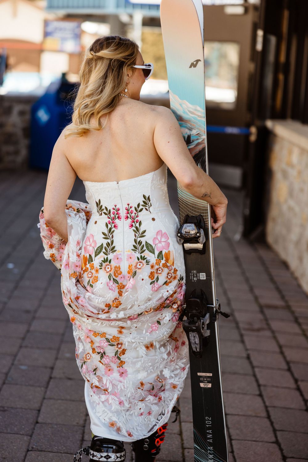 Back view of floral dress against ski equipment and stone building backdrop.
