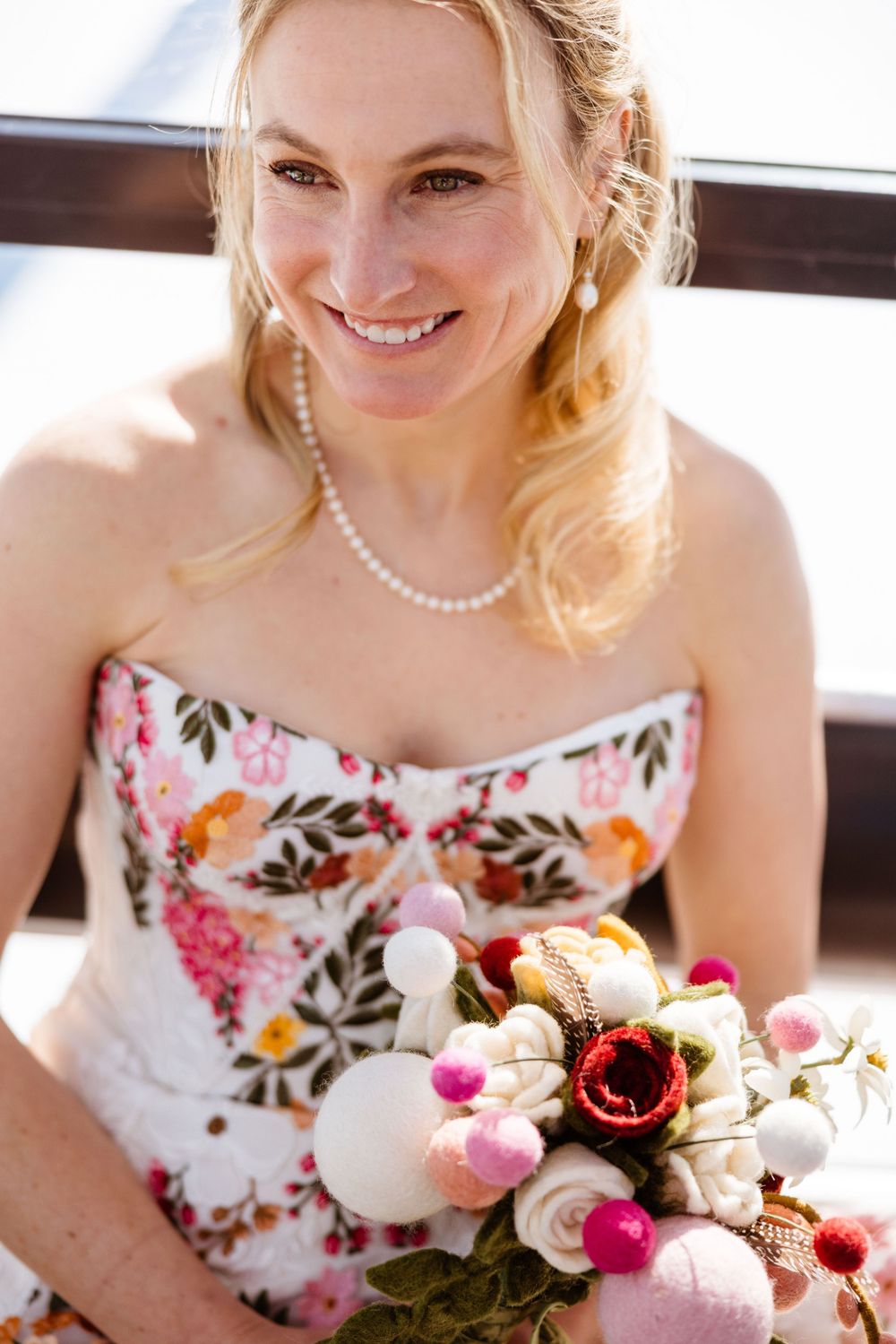 A floral wedding dress with embroidered details and a pearl necklace accessory.