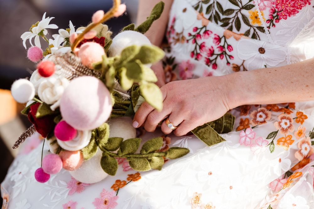 Close-up of a colorful bridal bouquet with pink and white flowers against a white dress.