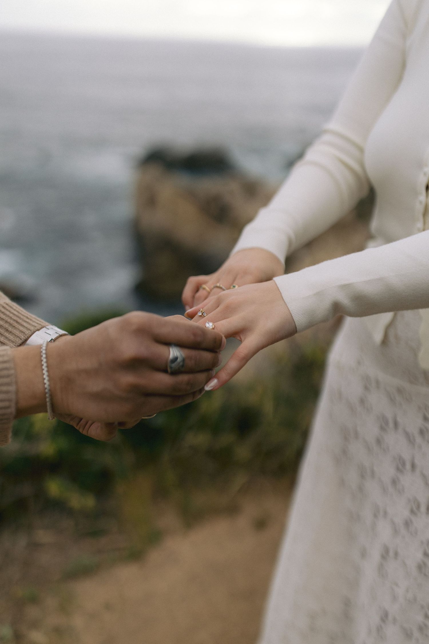 Close-up of hands exchanging rings during an outdoor seaside wedding proposal ceremony.