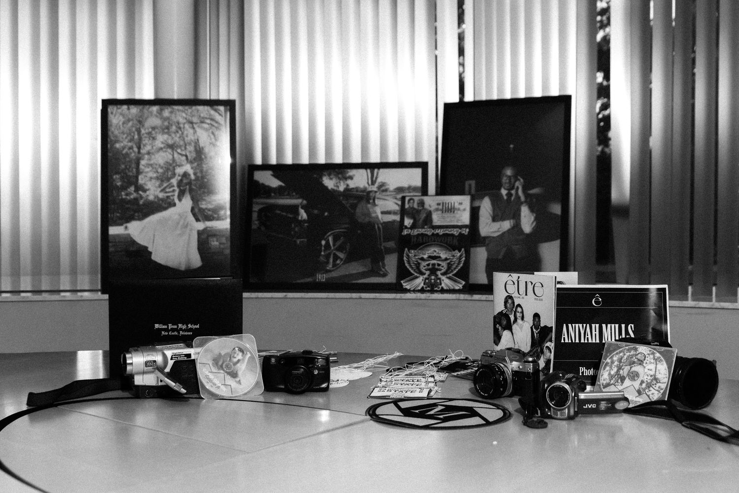 Black and white photo of a desk displaying framed photos, vinyl records, and vintage items including an Aniyah Mills album.