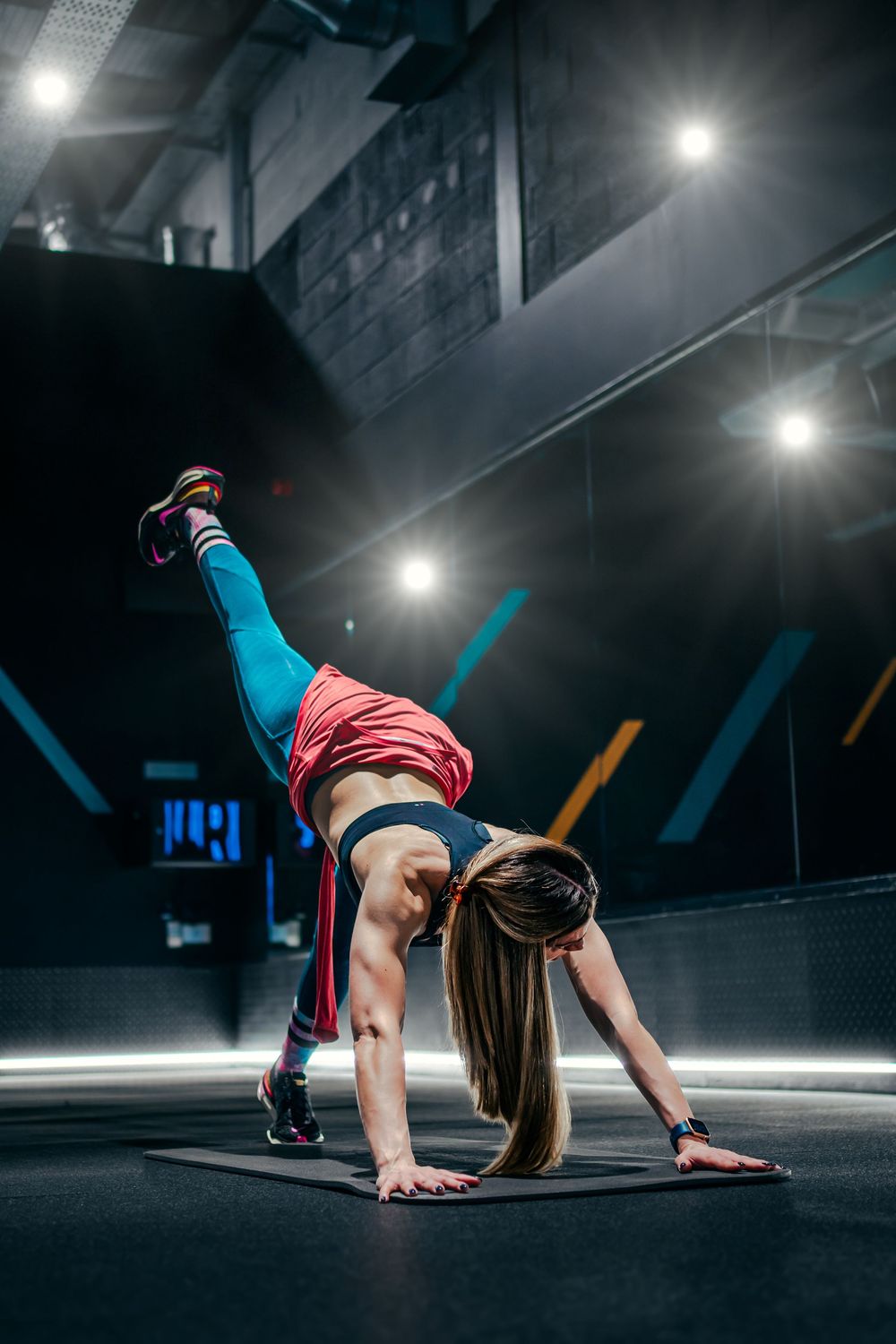 Dynamic workout pose with raised leg in colorful athletic wear at modern fitness facility.