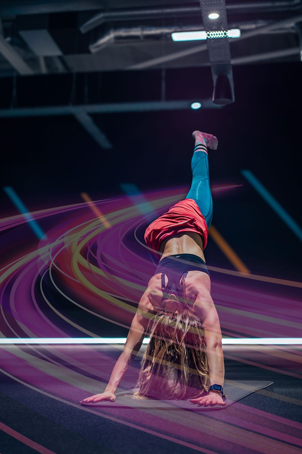 Dynamic shot of gymnast performing handstand with motion blur effects on colorful floor.