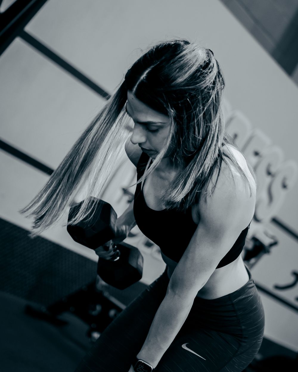Black and white gym photo showing dumbbell curl exercise in progress.