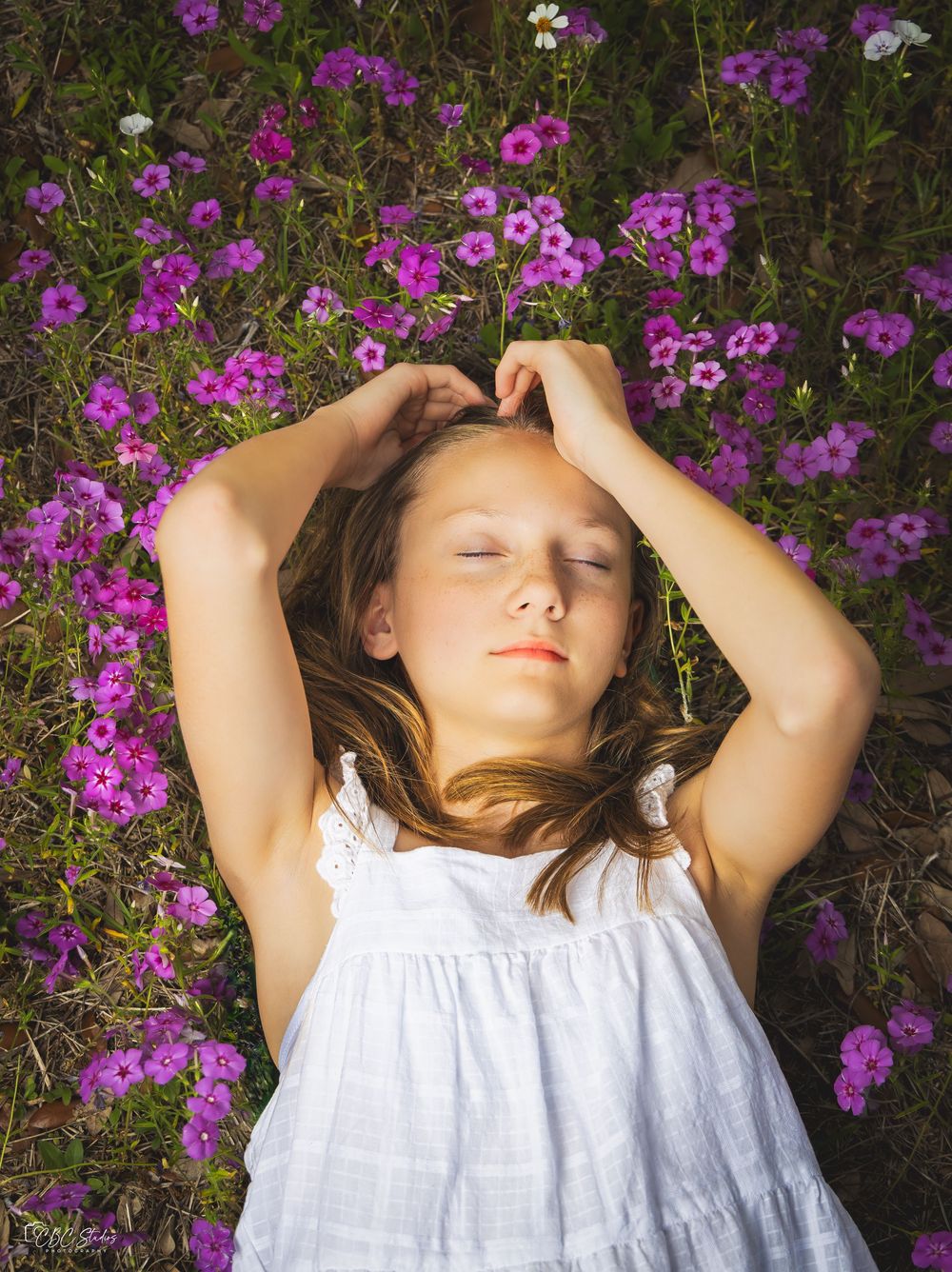 Person in white dress lying peacefully among vibrant purple wildflowers.