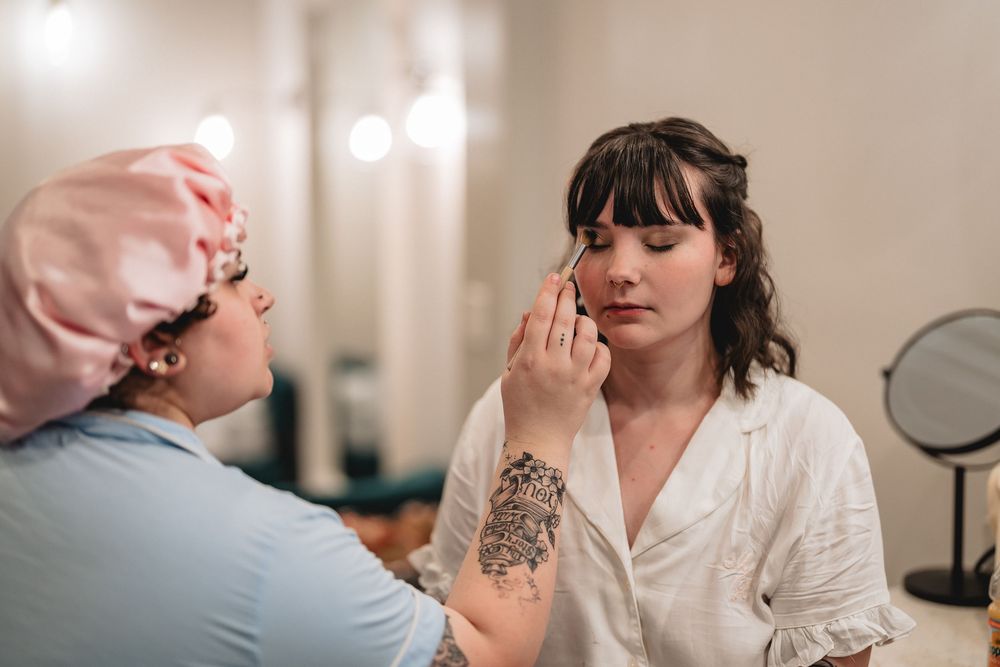 Professional makeup application in progress in a softly lit dressing room setting.