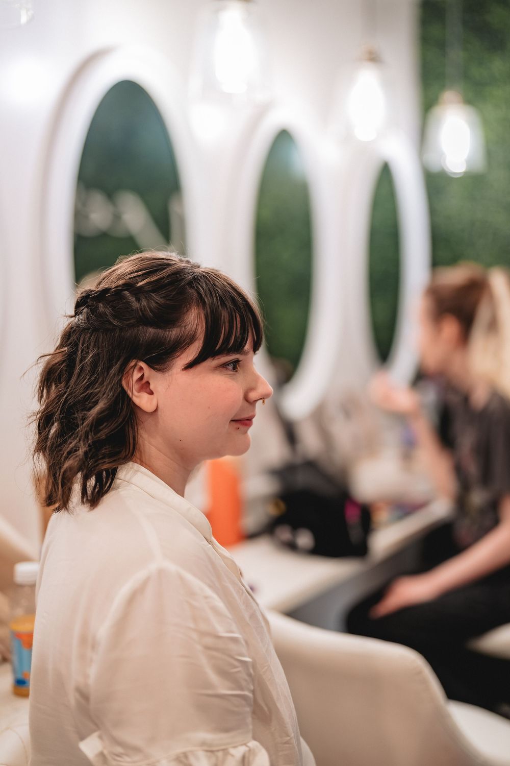 Side profile of someone getting their hair styled in a salon with circular mirrors and pendant lights.