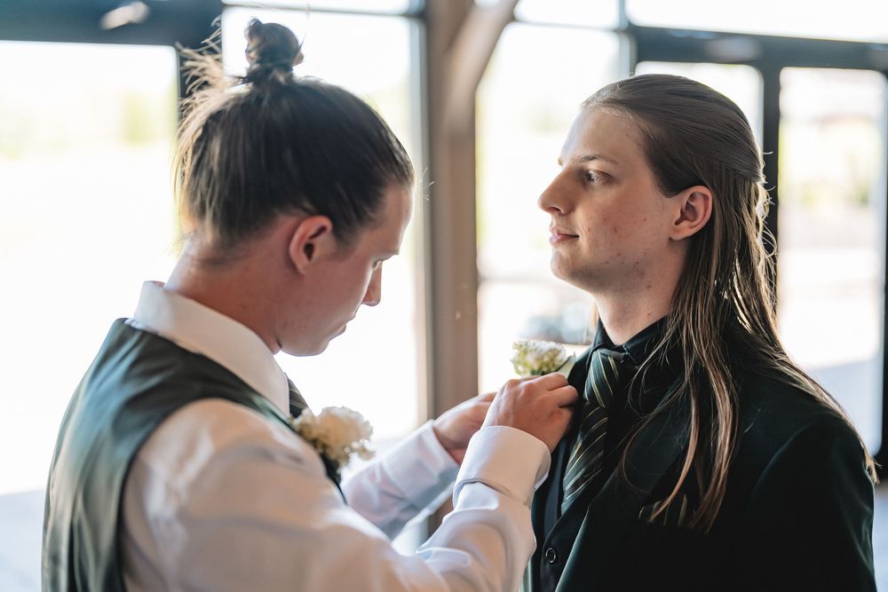 Two people adjusting formal attire and boutonniere during wedding preparations.
