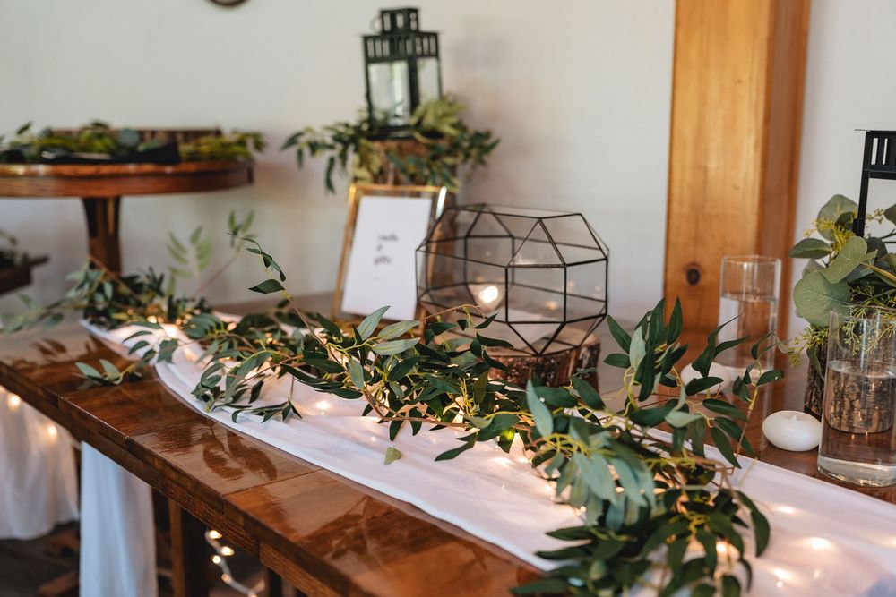 Rustic wooden table decorated with greenery, lanterns, and geometric terrariums for an elegant event display.