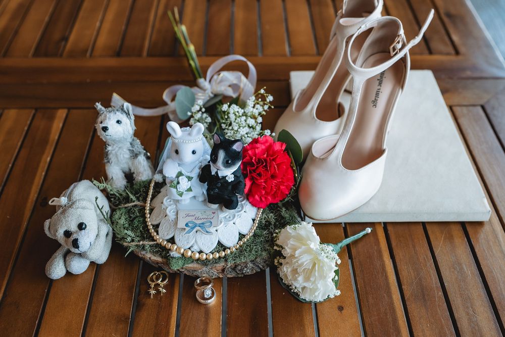 Wedding accessories including white shoes, decorative figurines, and floral arrangements on a wooden table.