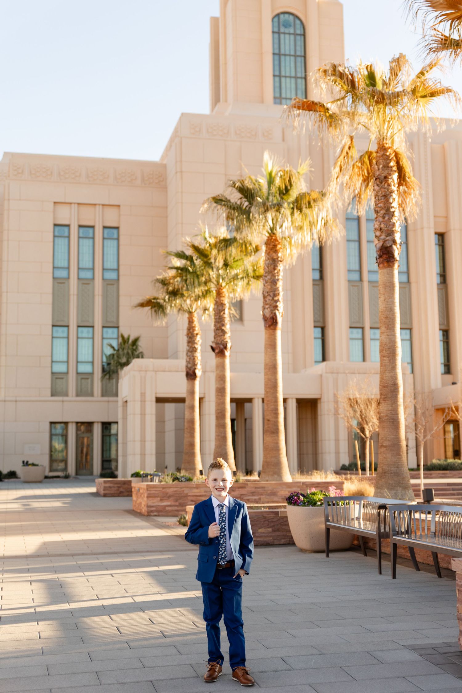 boy standing smiling at the camera in his blue suit in front of the temple with palm trees lining the way