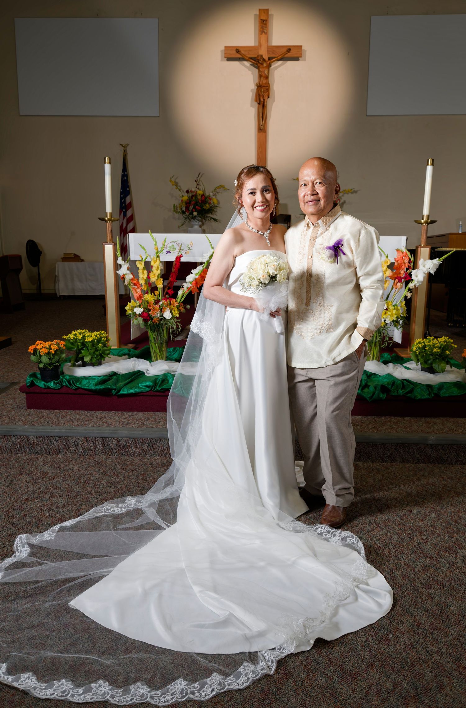 Two people in formal gowns, one in lavender and one in white with a flowing train, pose against an ivy-covered wall.