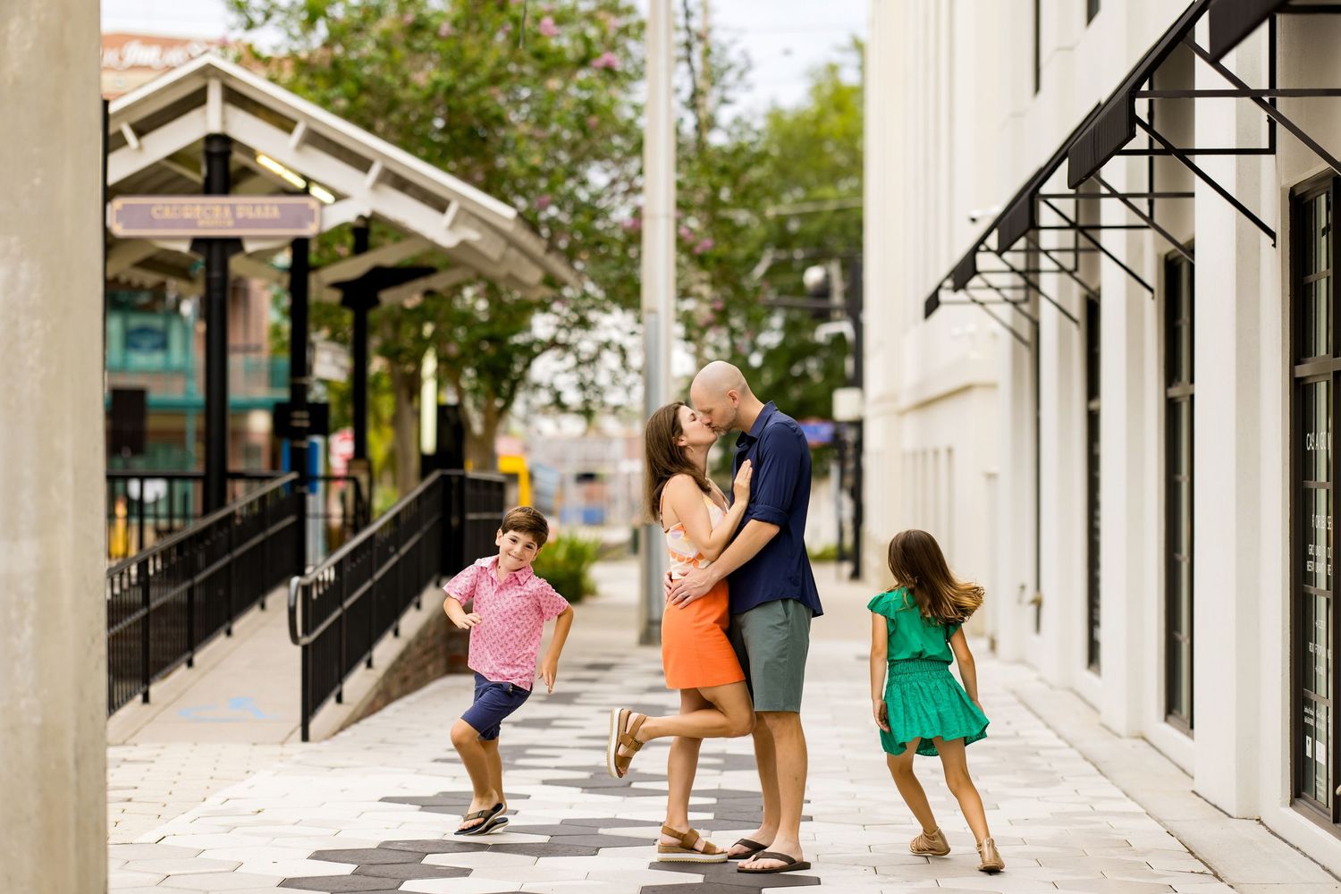 Urban sidewalk scene with brick buildings and casual pedestrians walking past storefronts.