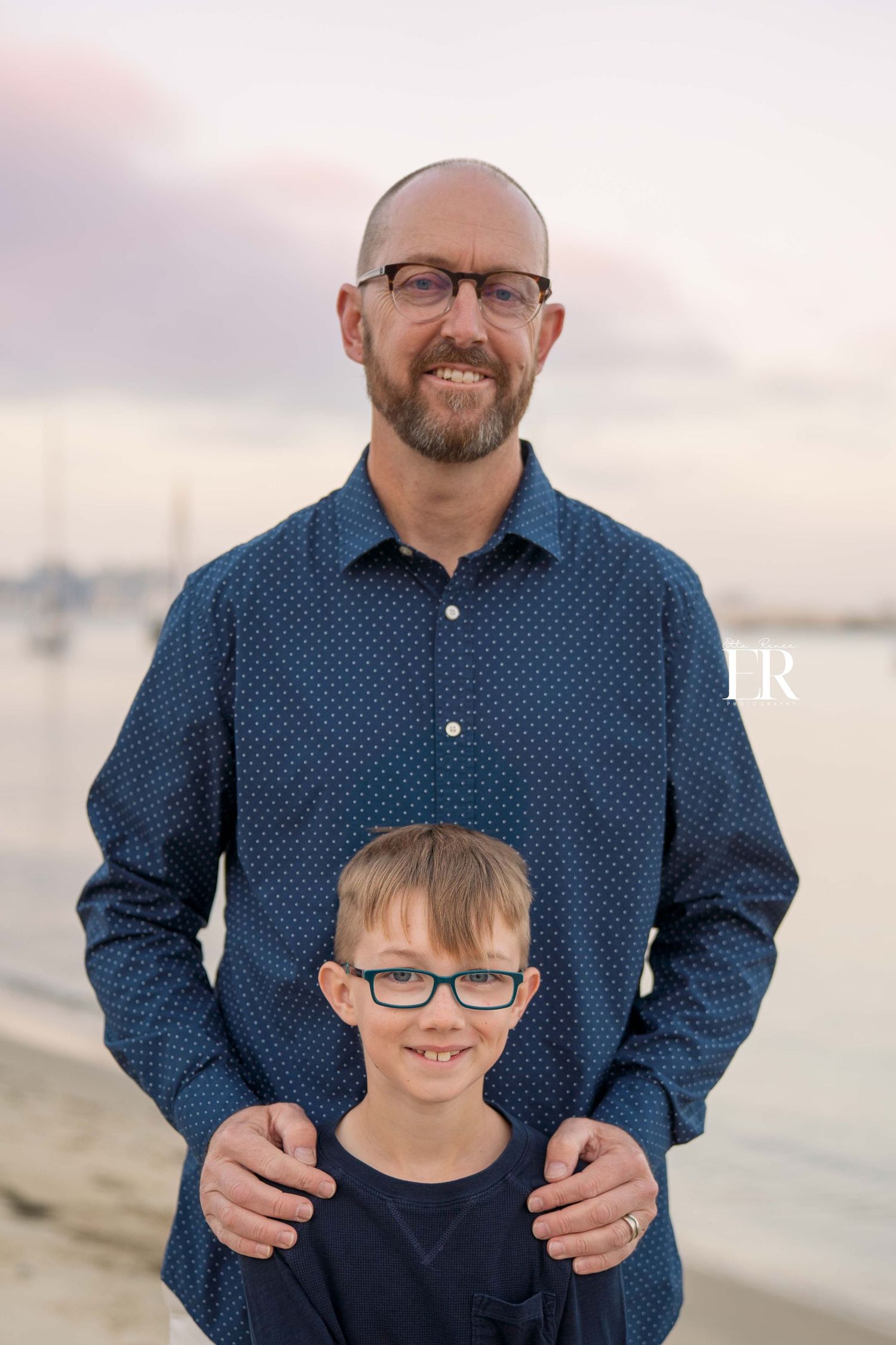 Portrait of two people on beach with soft sunset lighting in background.
