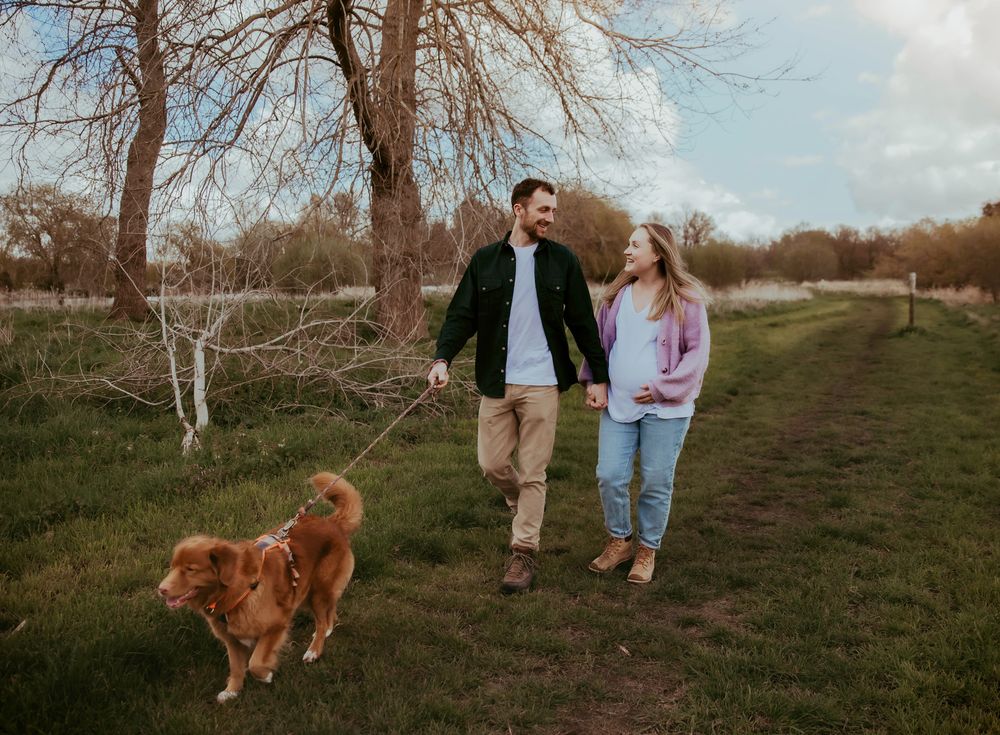 A couple walking their golden retriever dog on a nature trail during autumn with bare trees in the background.