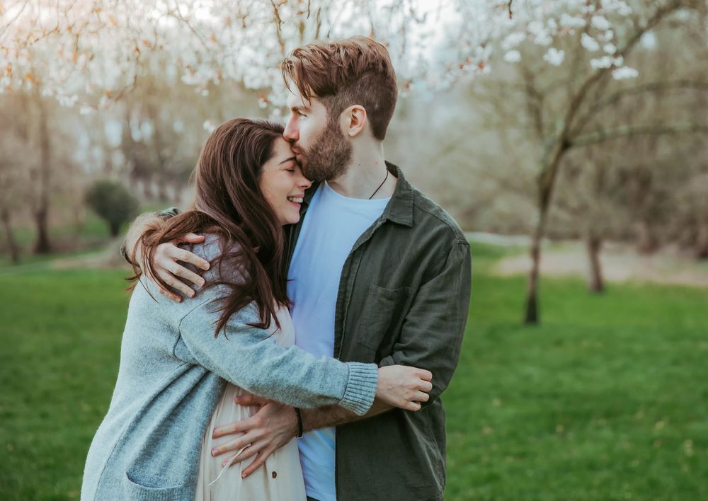 Young couple sharing a joyful embrace and laughter together on a green lawn in a park during spring.