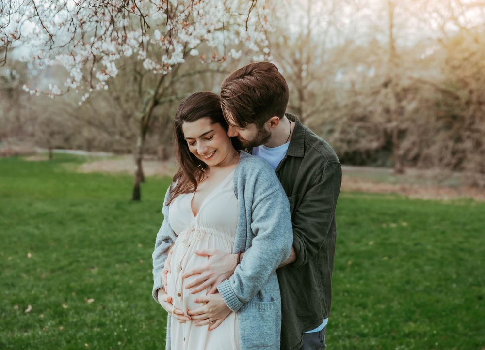 A loving couple shares a tender moment in a spring garden as they await their new arrival.